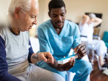 Een verpleegster laat een bejaarde zien hoe je een medicijndoosje gebruikt