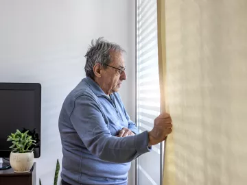 Een oudere persoon kijkt uit een raam